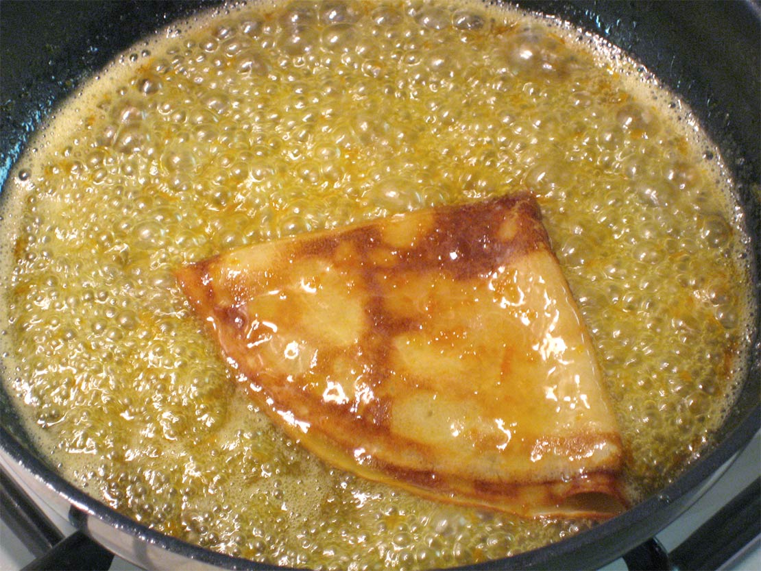 a folded crêpe in the sauce in the frying pan